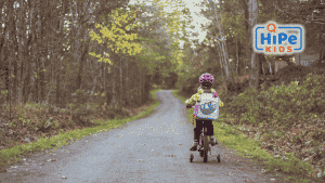 Petite fille sur un vélo à roulettes avec un sac à dos sur un chemin.