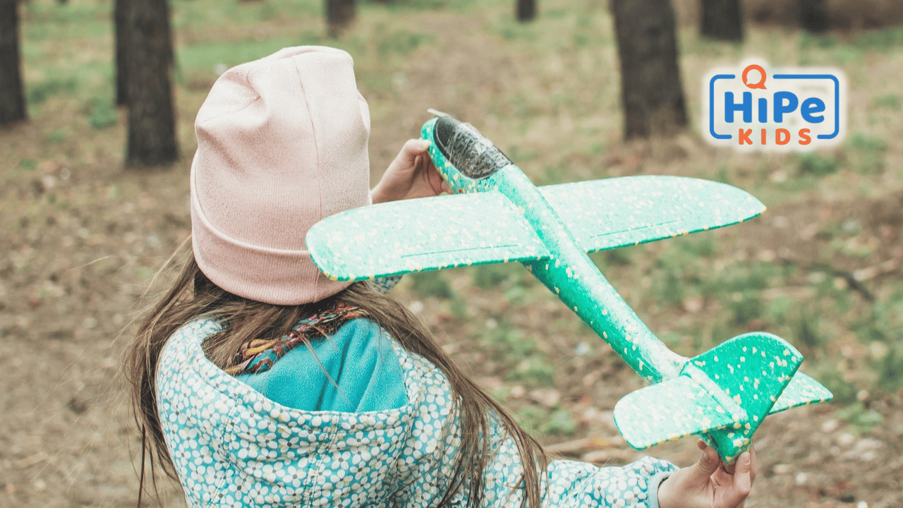 Petite fille de dos avec un bonnet rose sur la tête sur le point de lancer un avion en jouet.