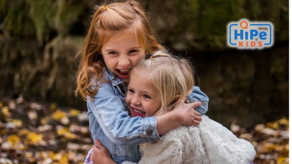 Deux petites filles se font un câlin sur fond de feuilles mortes.
