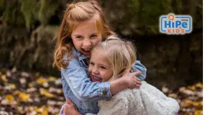 Deux petites filles se font un câlin sur fond de feuilles mortes.